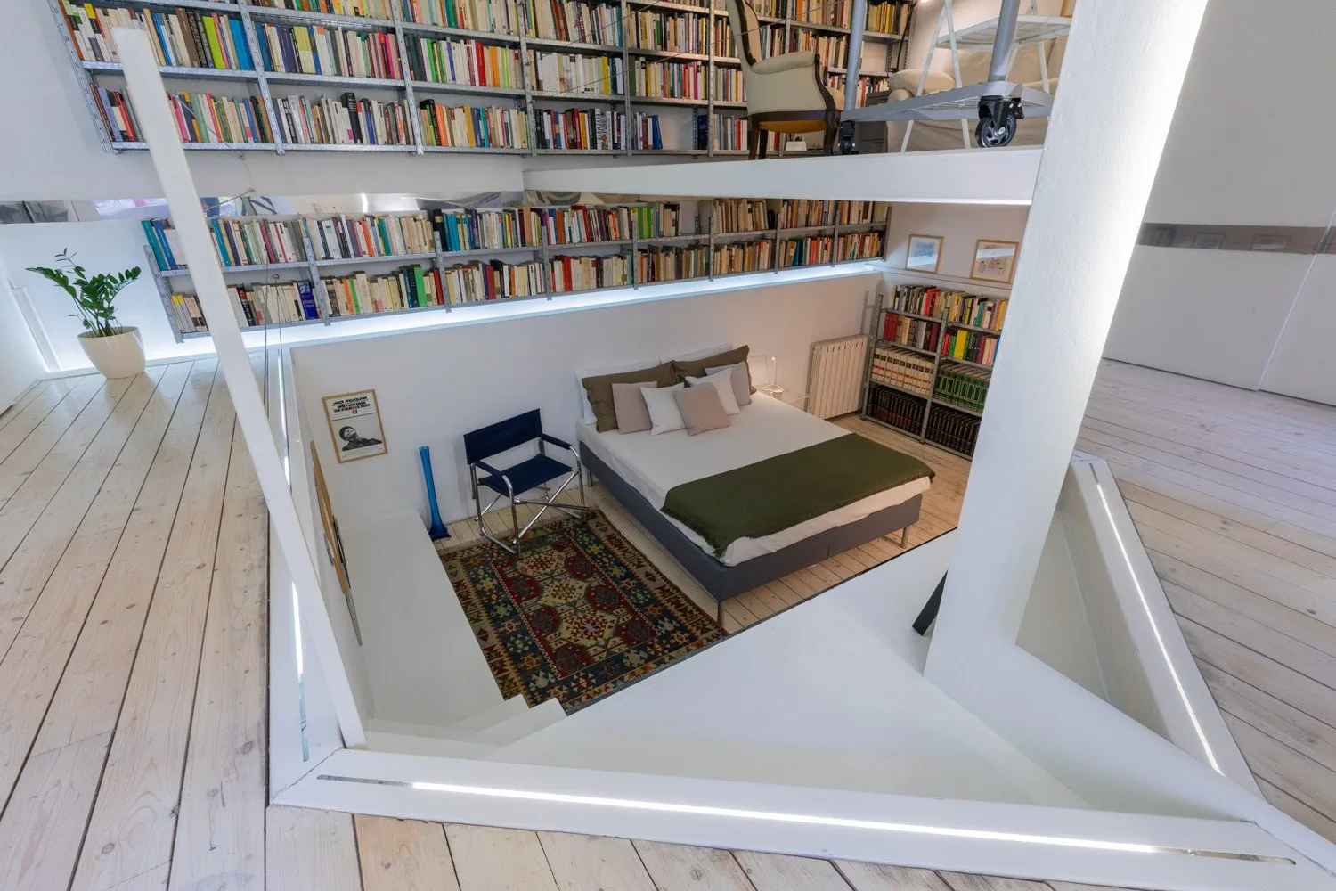 Un dormitorio bajo estanterías altas, con una cama y una pequeña zona de asientos.