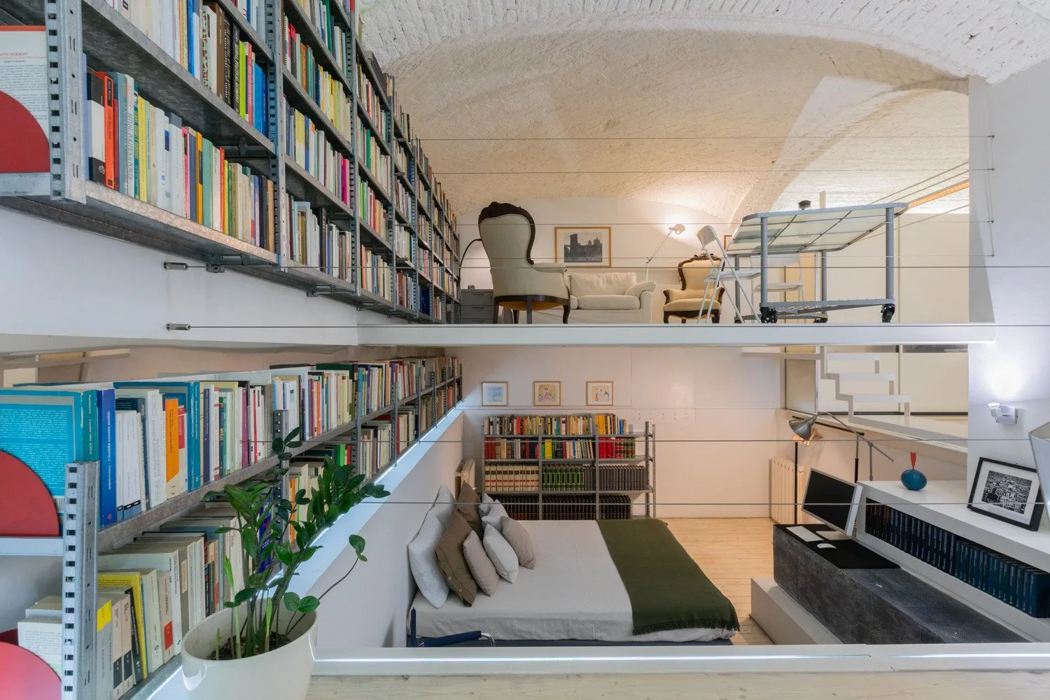 Un espacio de estar tipo biblioteca con estanterías, asientos y un altillo.