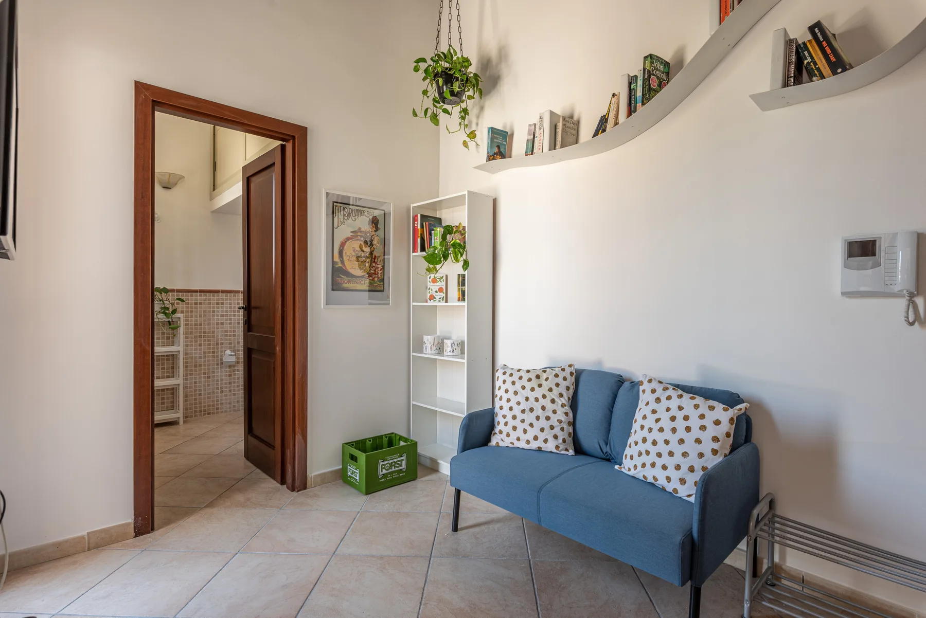 Una sala de estar con asientos azules, estantes en la pared y una puerta abierta.