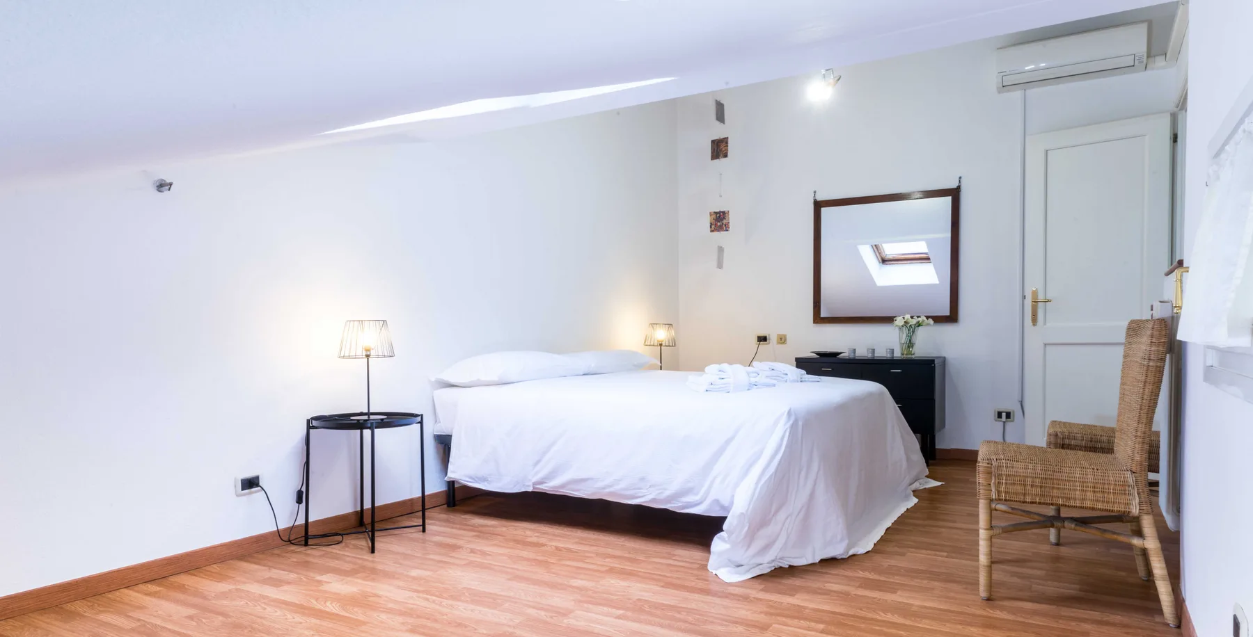 A bright bedroom with a neatly made bed, bedside tables, and a wall mirror.
