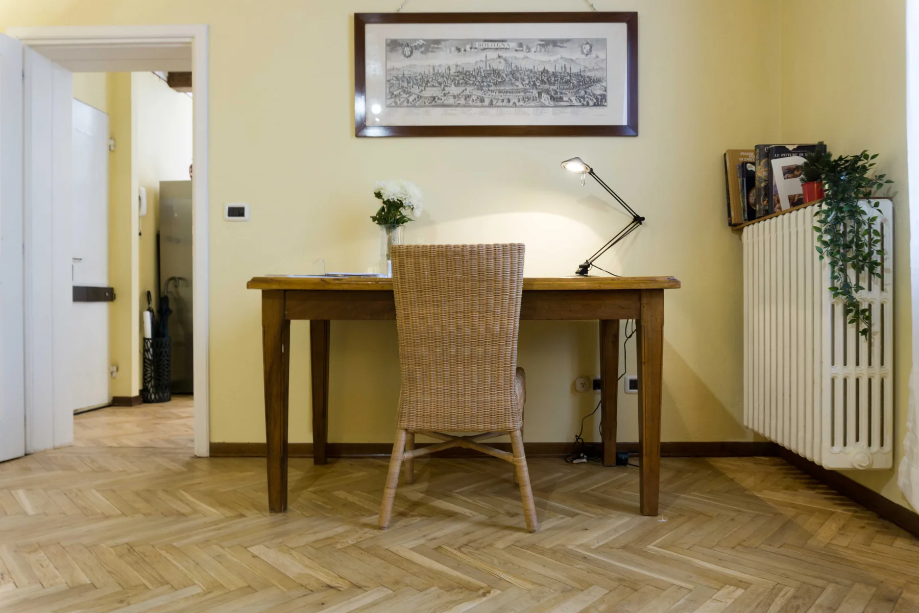 A wooden desk and woven seating sit beneath framed artwork in a bright room.
