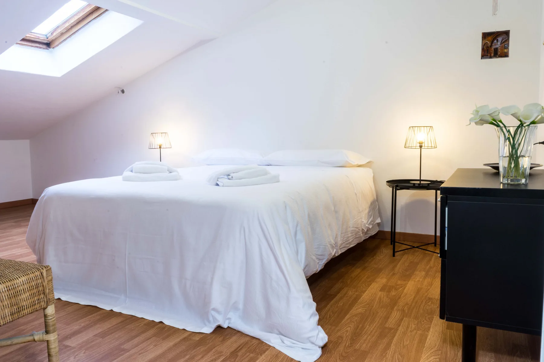 A bedroom with a large bed beneath a sloped ceiling and skylight.