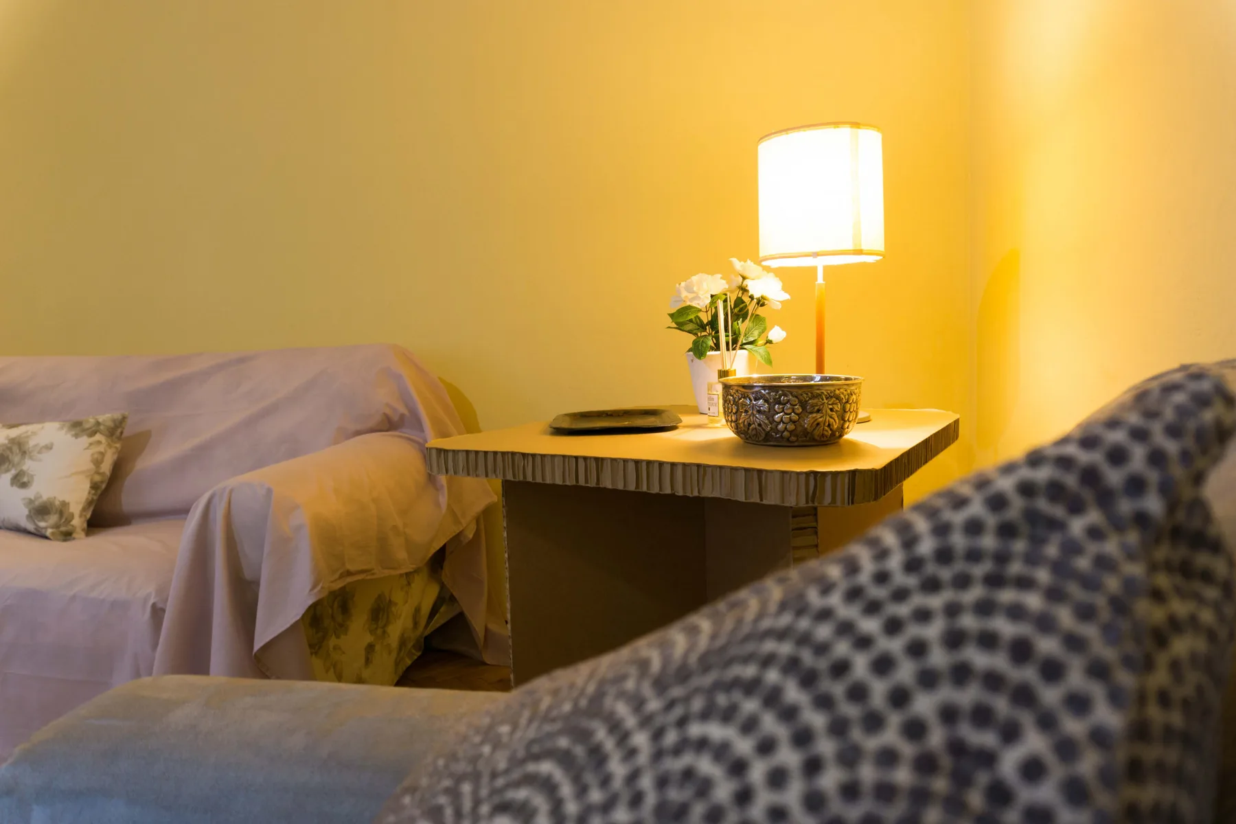 A warmly lit sitting area with a side table, lamp, and seating.