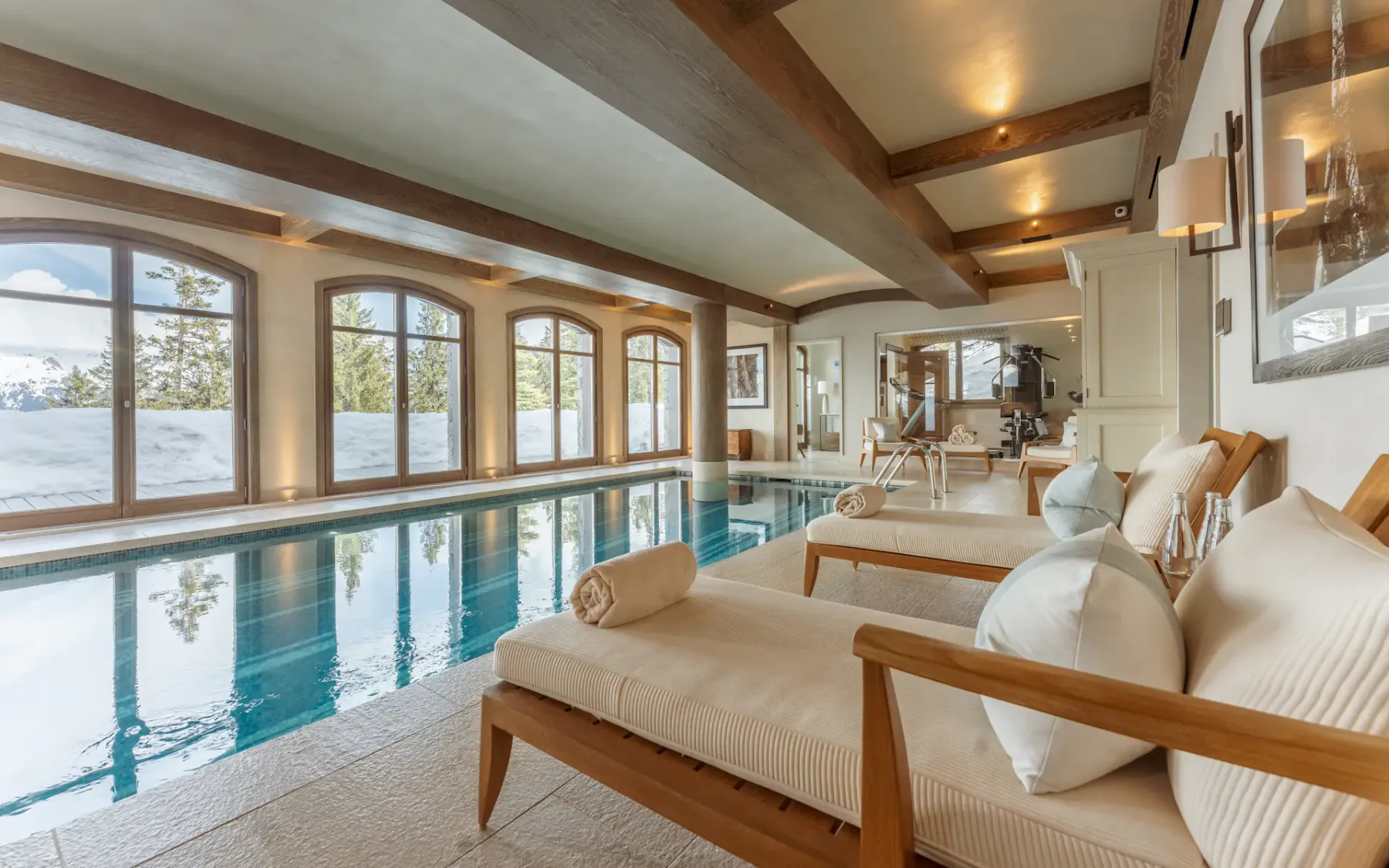 Una piscina cubierta junto a asientos acolchados, con ventanas arqueadas que dan a un paisaje nevado.