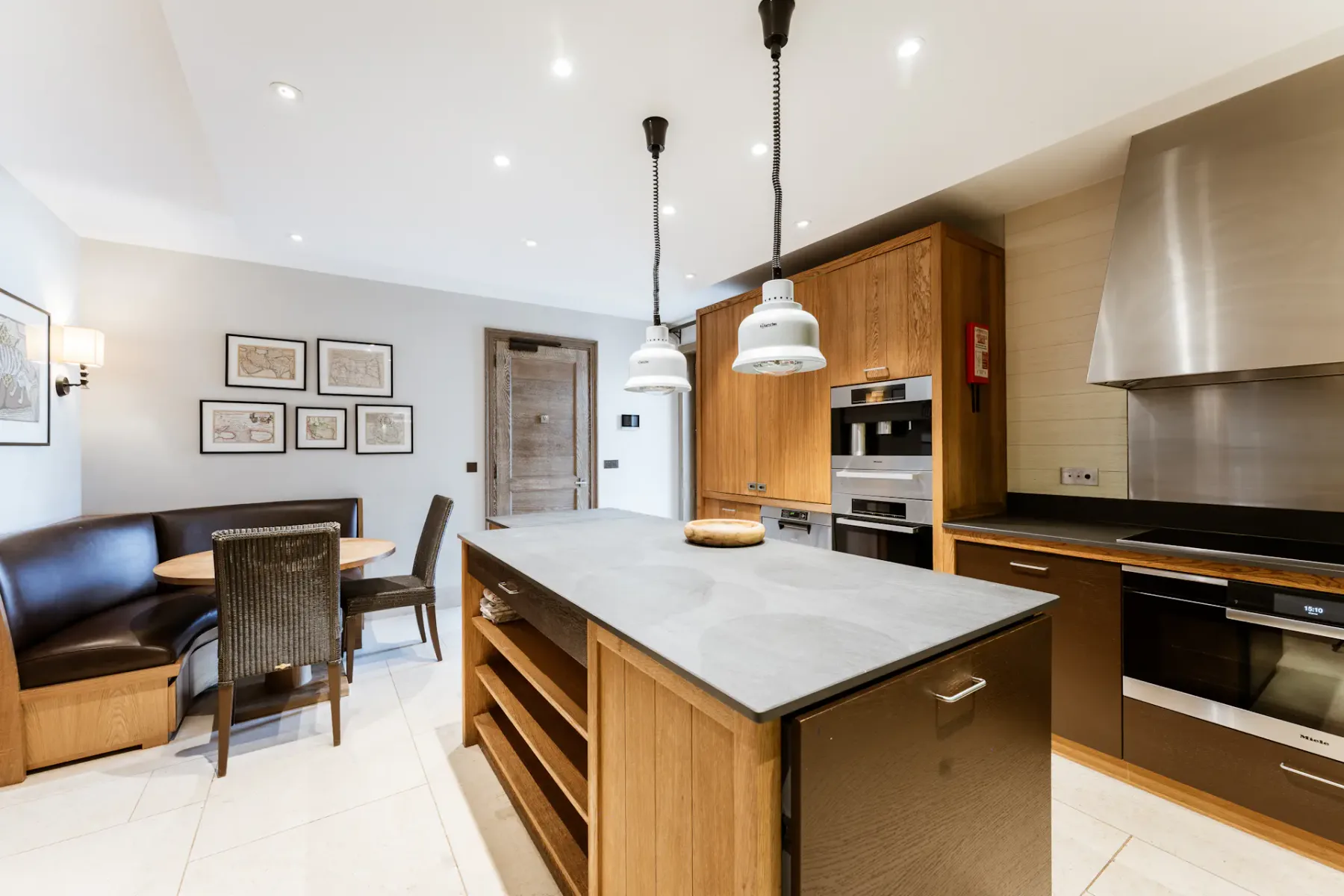 Cocina moderna con armarios de madera, una isla central, electrodomésticos de acero inoxidable y un acogedor rincón de comedor con mesa redonda y sillas.