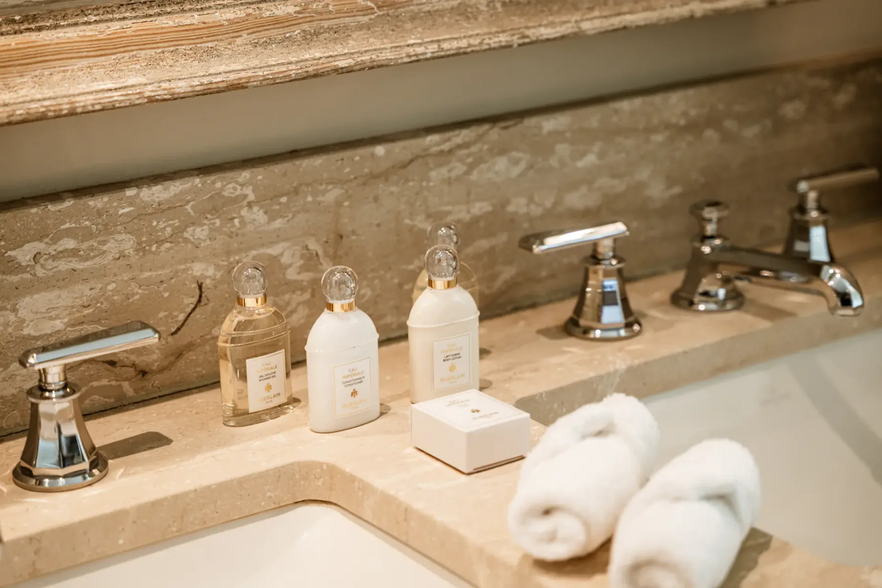 Un tocador de baño muestra varios frascos de aseo junto a toallas blancas enrolladas.