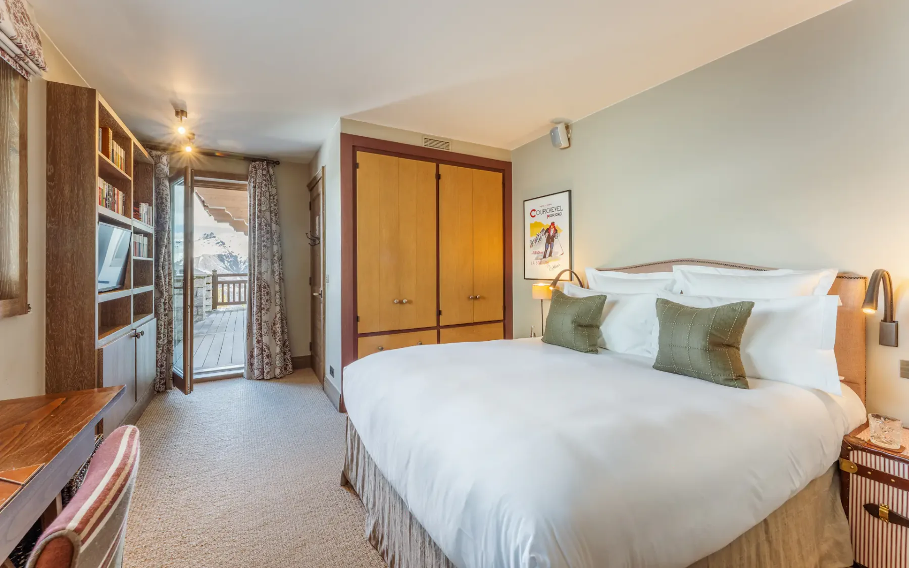 Acogedor dormitorio con una cama grande, una pared decorativa de madera, televisor y una ventana con cortinas que da a un balcón con árboles en el exterior.
