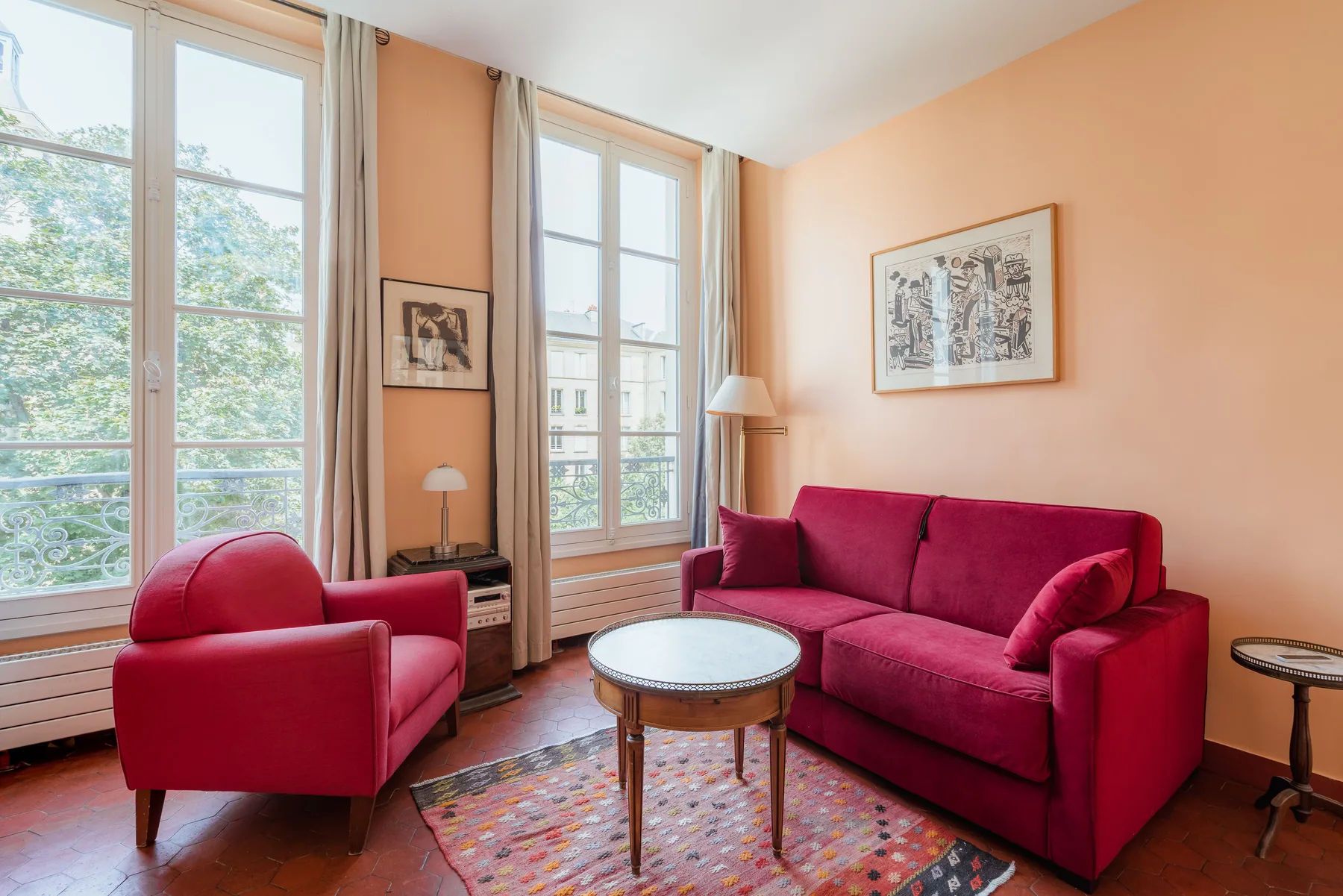 A living room with red seating, a coffee table, and tall windows.