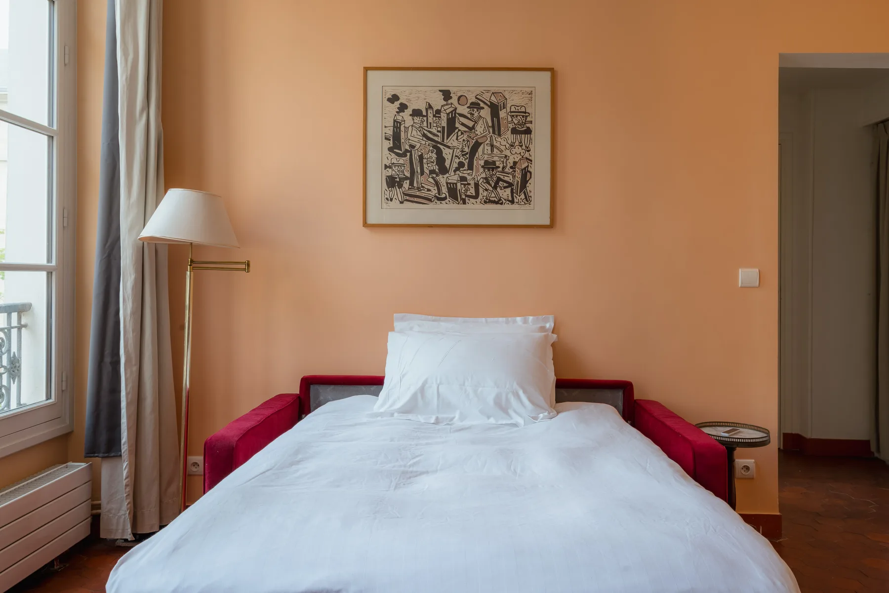 A bedroom with a bed, red seating, and framed artwork on the wall.