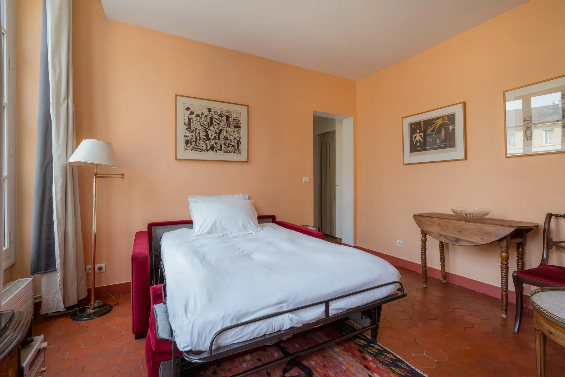 A bedroom with a bed, peach-colored walls, and framed artwork.