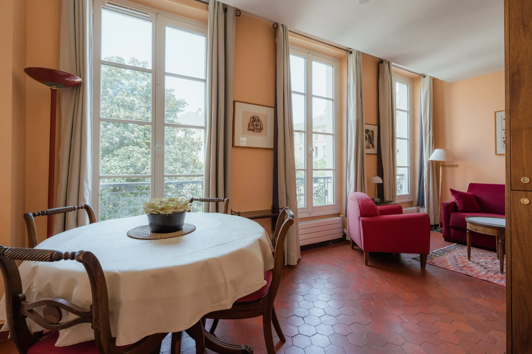 A bright sitting and dining room with tall windows and red seating.