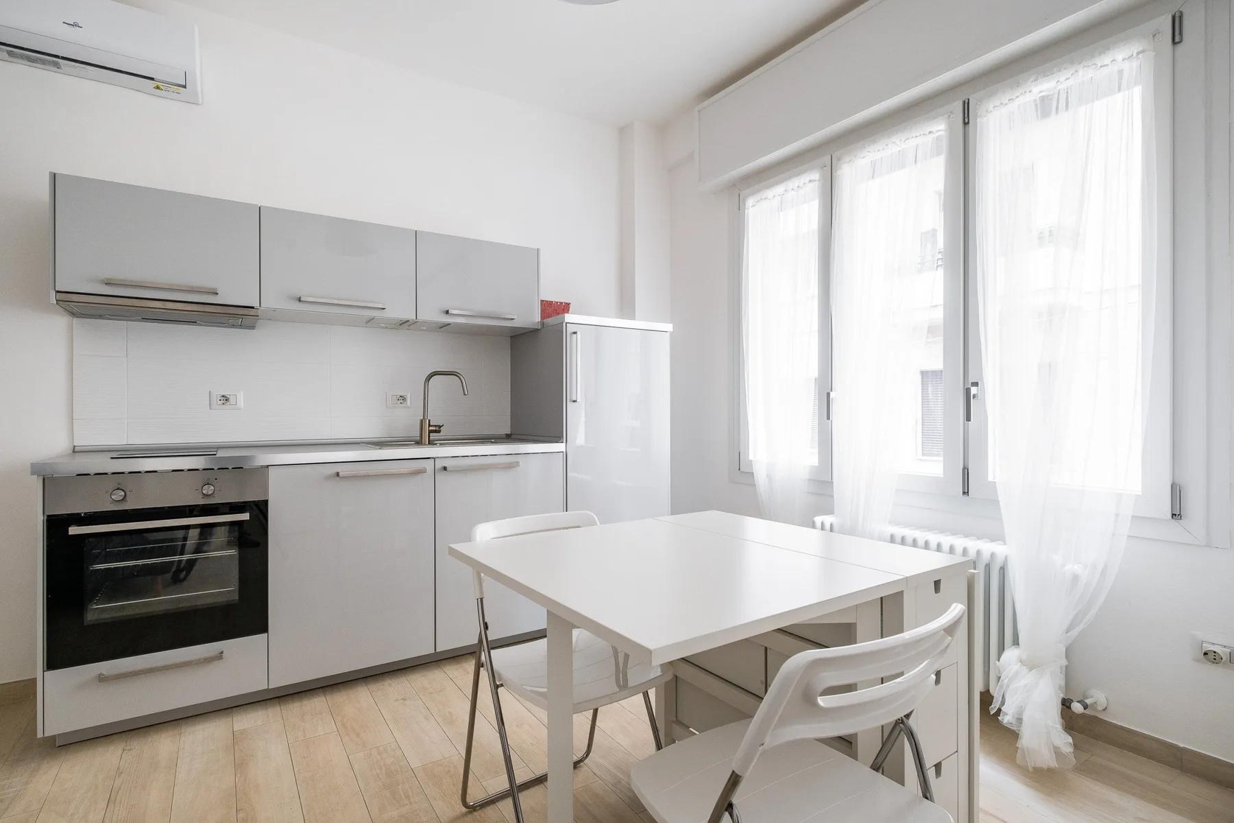 A bright kitchen and dining area with white cabinetry, a table, and large windows.