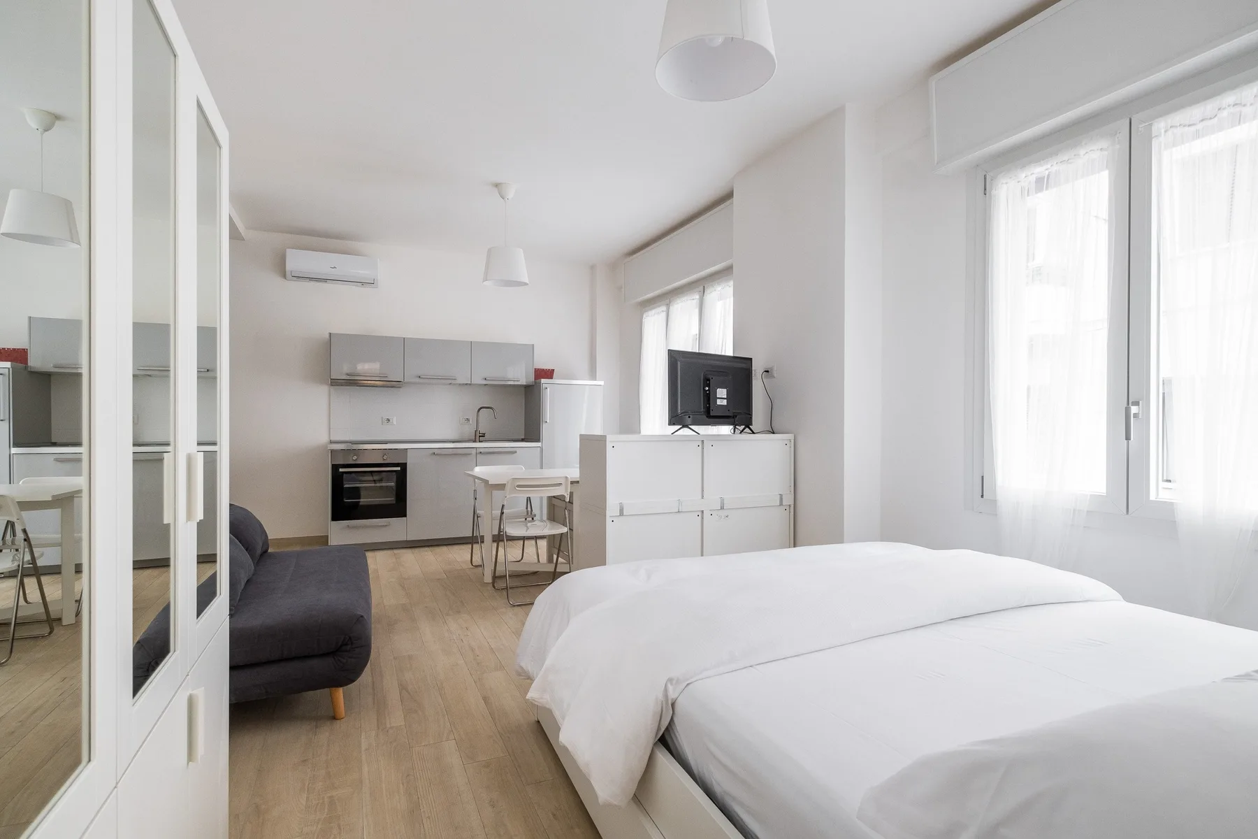 A bright bedroom with two beds and a small kitchen area.