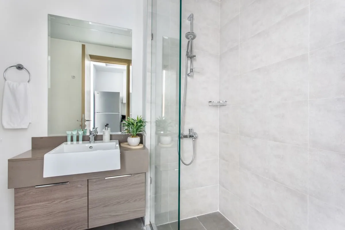 Un baño luminoso con lavabo, espejo y ducha de cristal.