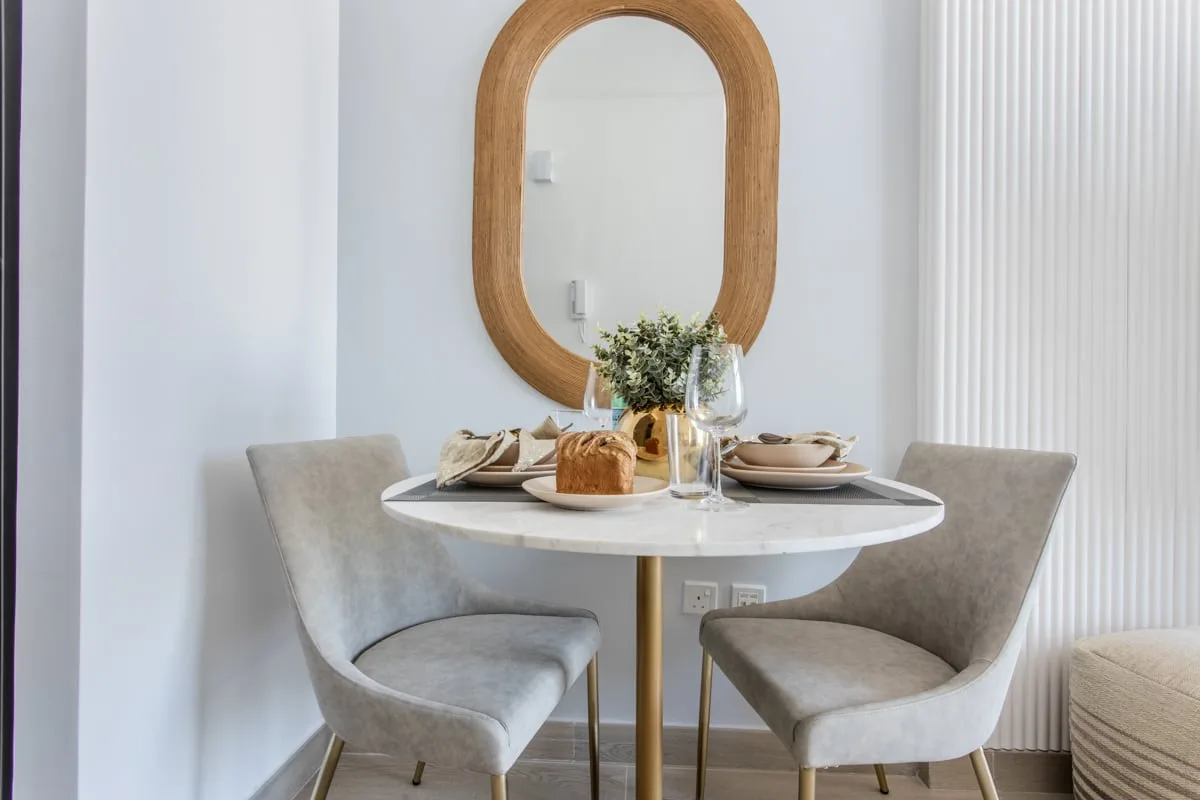 Un comedor con una mesa redonda preparada para comer junto a un espejo ovalado.