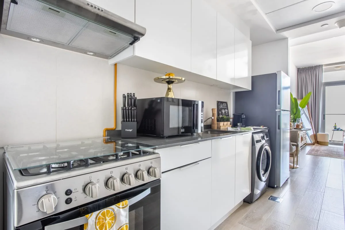 Una cocina luminosa y moderna con gabinetes blancos, electrodomésticos de encimera y una lavadora.