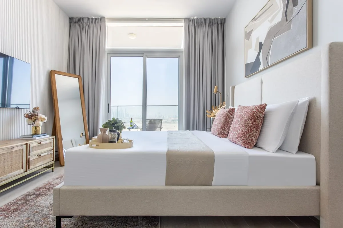 Un dormitorio luminoso con una cama bien tendida y grandes ventanas.