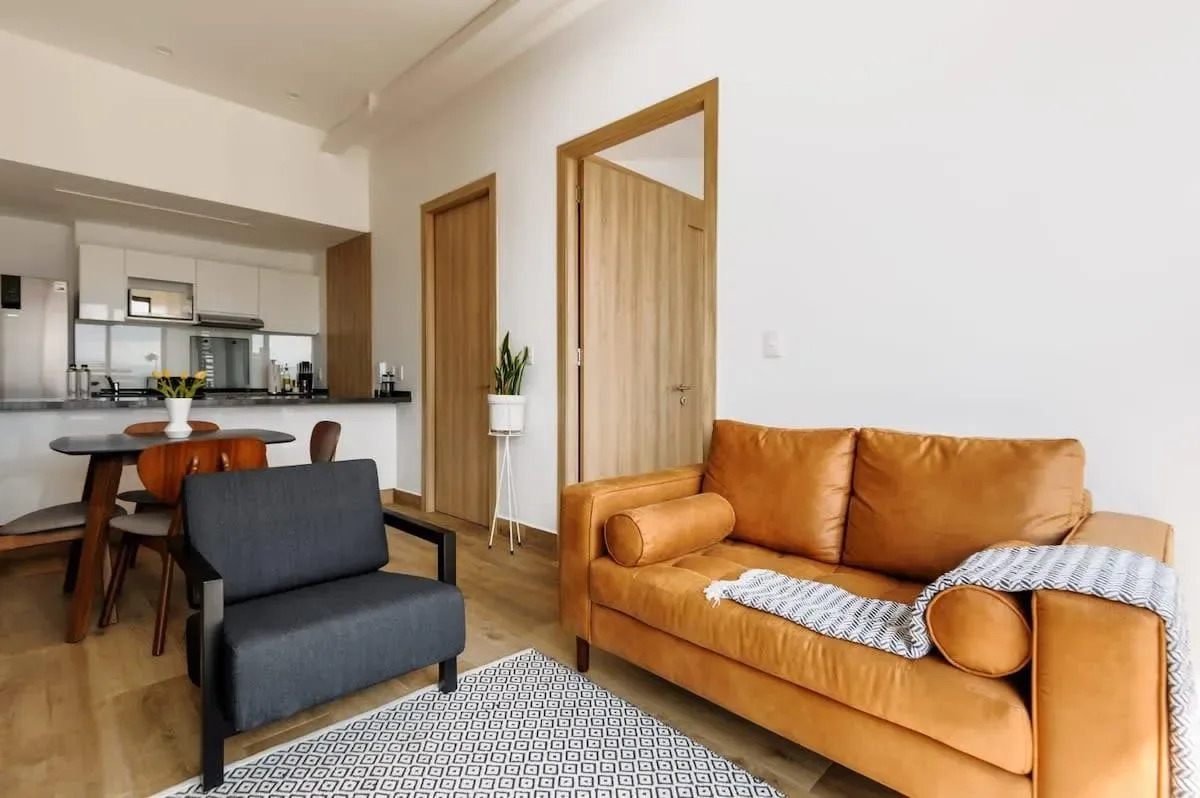 A living room with an orange sofa, a dark armchair, and an open kitchen.