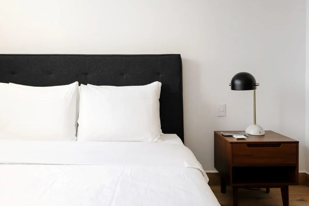 A neatly made bed with white bedding and a dark headboard beside a wooden nightstand.