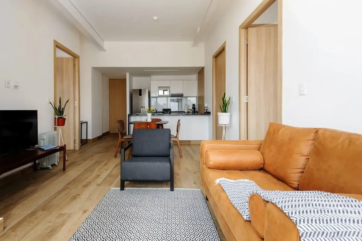 A living room with seating, a television, and an open kitchen in the background.