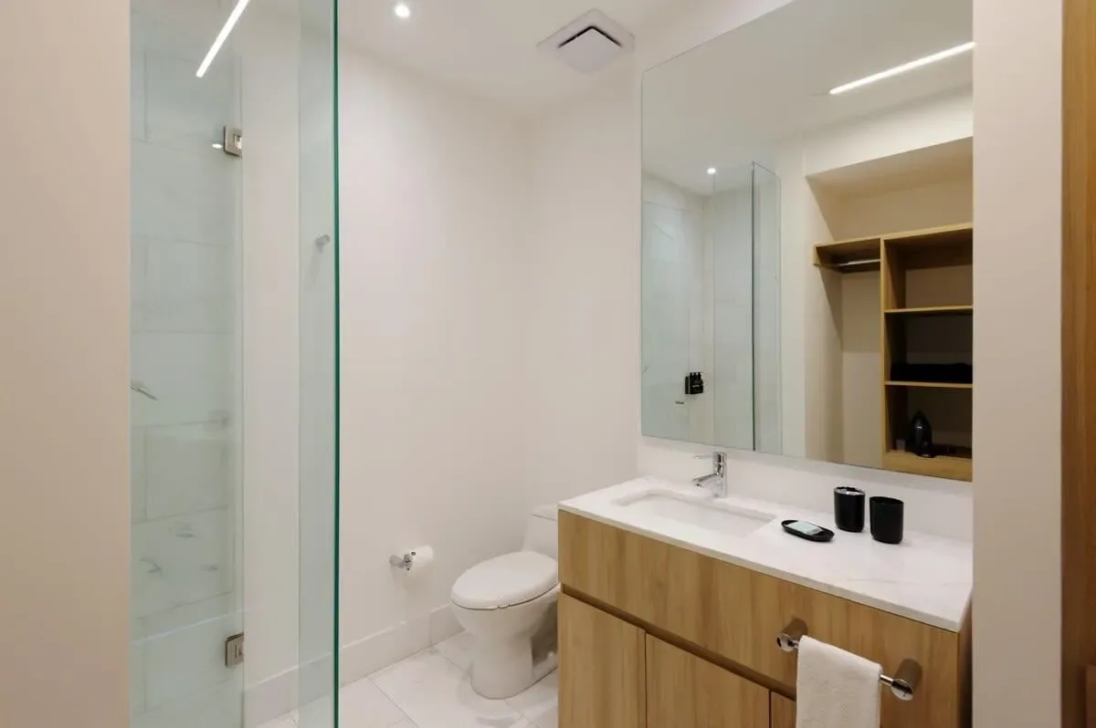 A bright bathroom with a glass shower, toilet, and wood vanity.