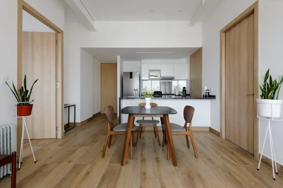 A dining area with a wooden table and chairs opens onto a compact kitchen.