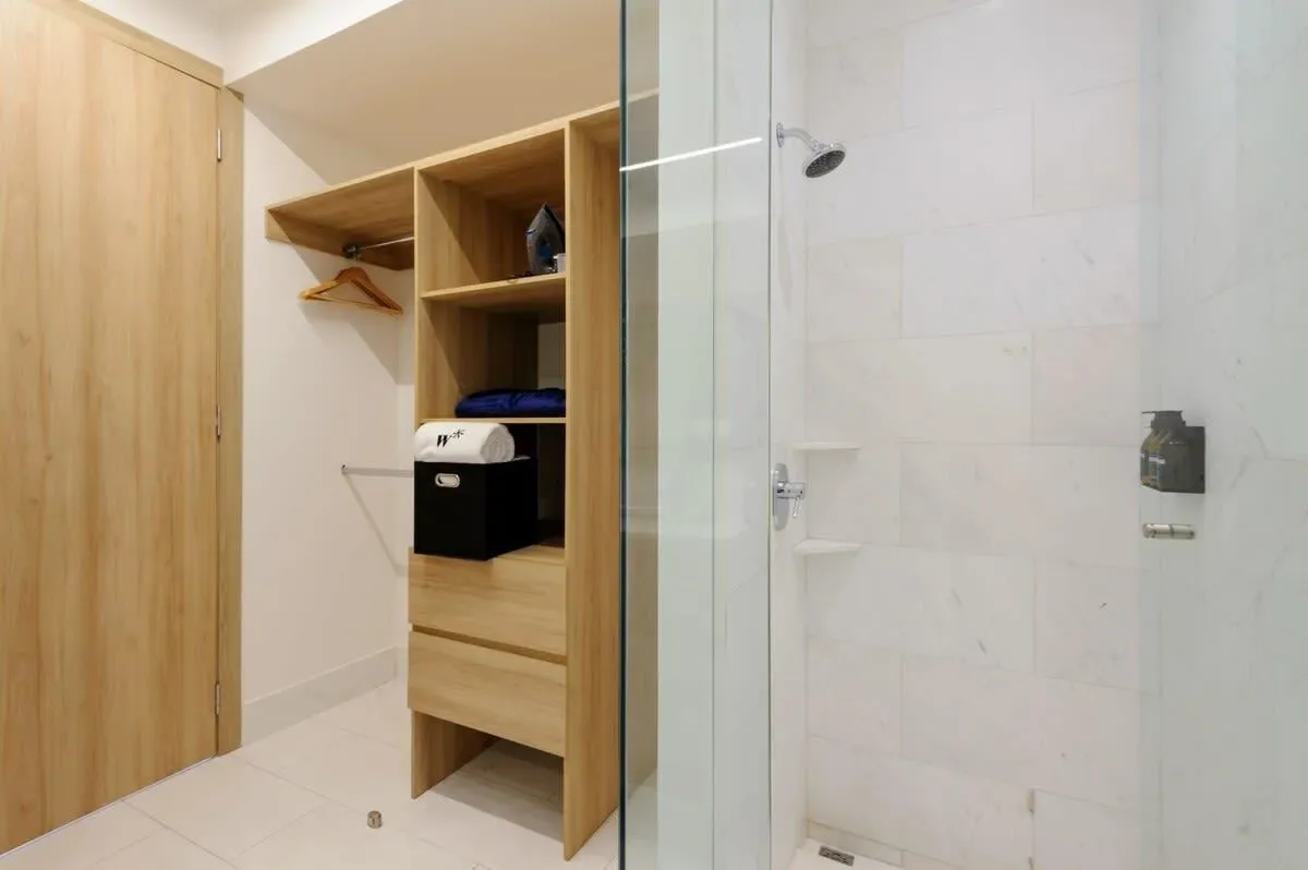 A bathroom with a glass shower beside a wooden storage unit.