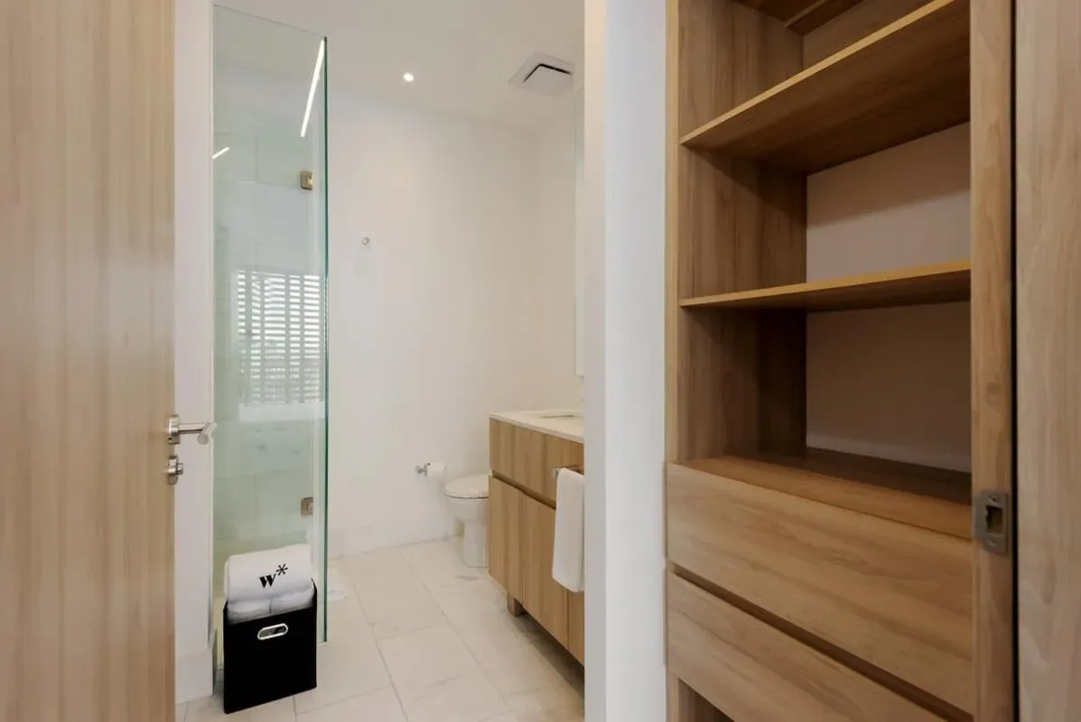 A bathroom with a glass shower and wooden storage cabinets.