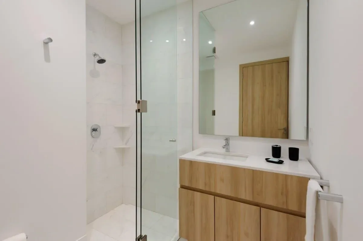 A bright bathroom with a glass shower and a wood-fronted vanity.