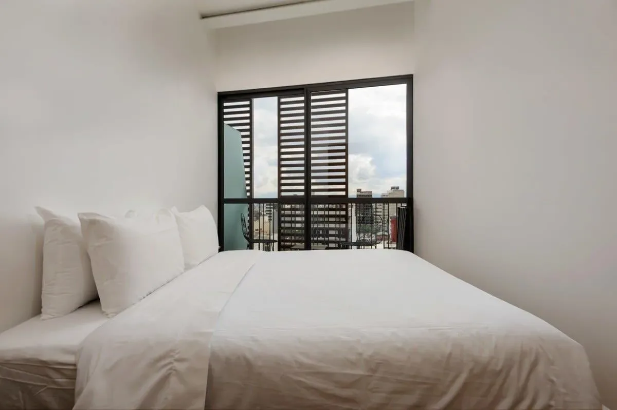 A bright bedroom with a white bed facing a large window.