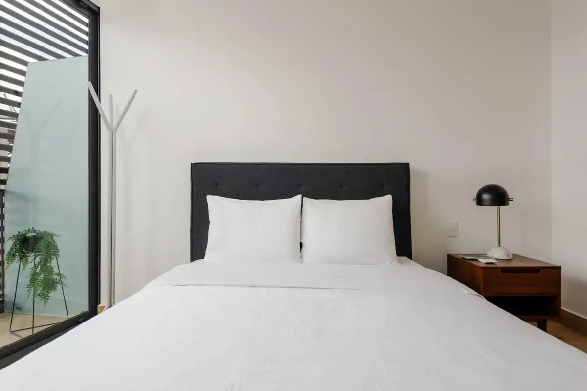 A bedroom with a bed, white bedding, and a dark headboard.