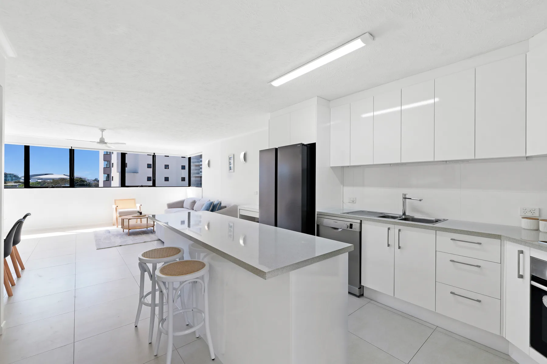 A bright kitchen with a long island and dining seating beside wide windows.