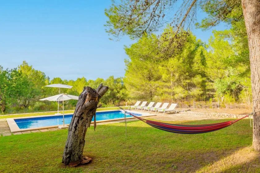 An outdoor pool beside a grassy yard with a hammock and lounge chairs.