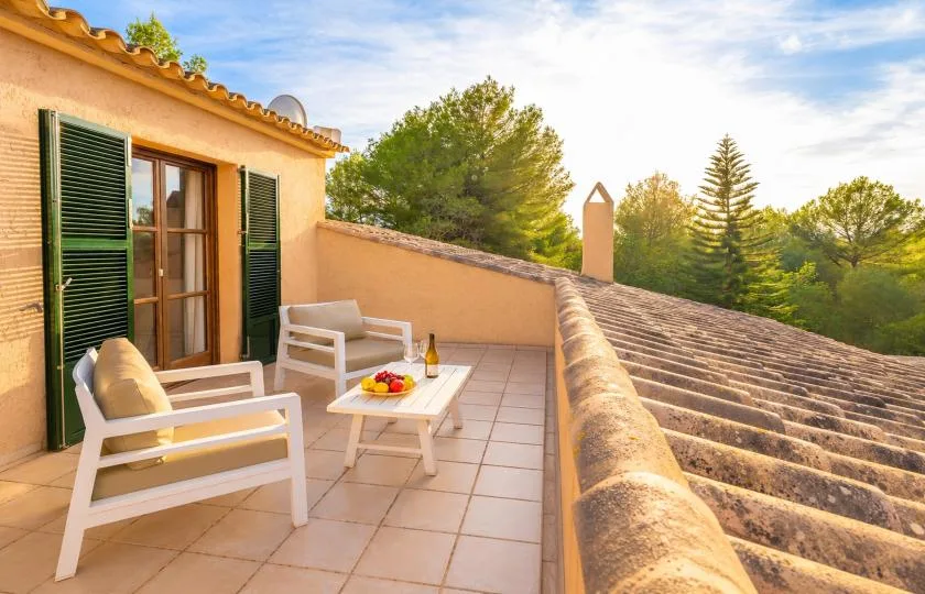 A tiled terrace with outdoor seating overlooks a roof and surrounding trees.