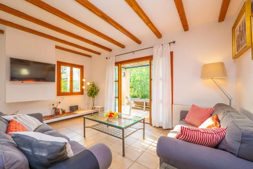 A bright living room with seating around a glass coffee table and open patio doors.