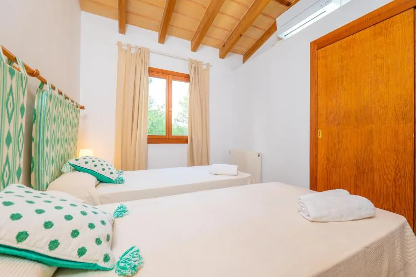 A bedroom with two beds, patterned bedding, and a window beneath a wooden ceiling.