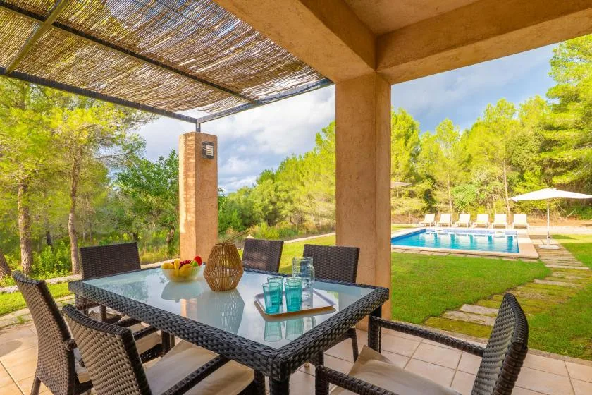 A covered outdoor dining area overlooks a swimming pool and green landscaping.