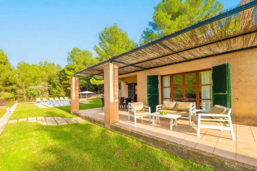 A covered patio with outdoor seating overlooks a grassy lawn and swimming pool.