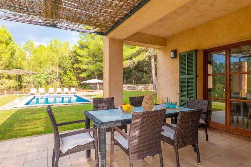 A covered outdoor dining area overlooks a swimming pool and garden.