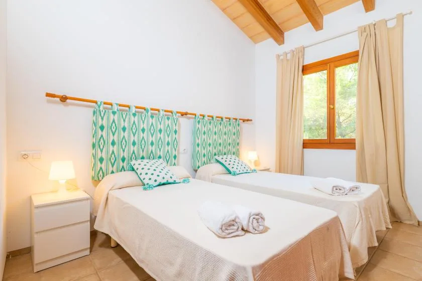 A bright bedroom with two beds, patterned curtains, and a wooden ceiling.