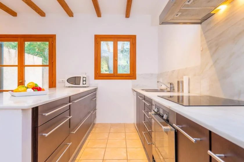 A bright kitchen with wood cabinetry, white countertops, and windows.