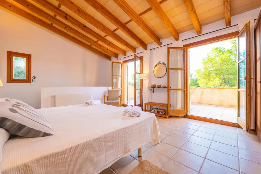 A bright bedroom with a bed and open glass doors leading to a terrace.