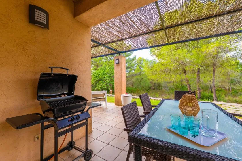 A covered patio has a dining table and an open barbecue grill.