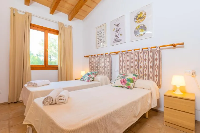 A bright bedroom with two beds, patterned cushions, and a wooden ceiling.