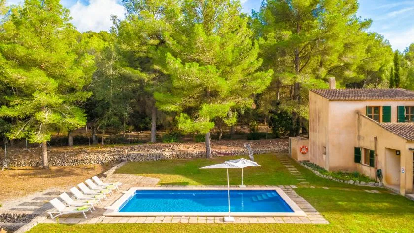 An outdoor swimming pool sits beside a building and tree-lined lawn.