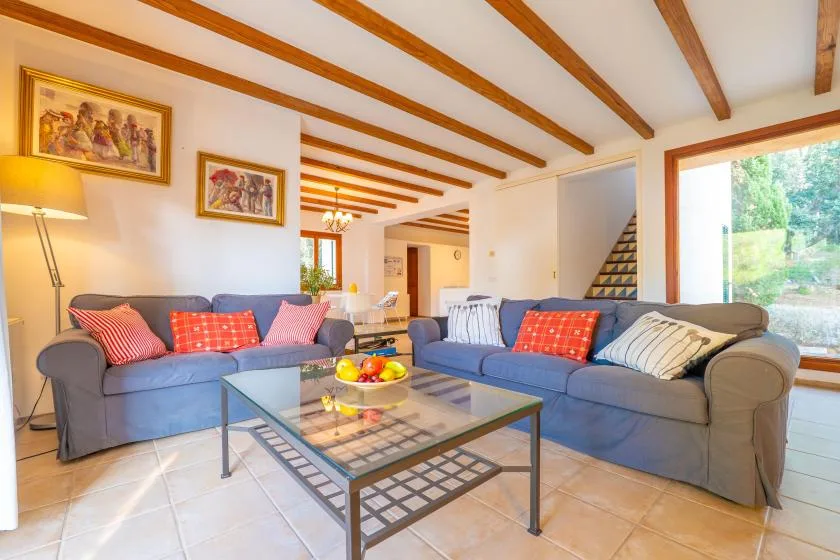 A living room with blue seating, a glass coffee table, and exposed ceiling beams.