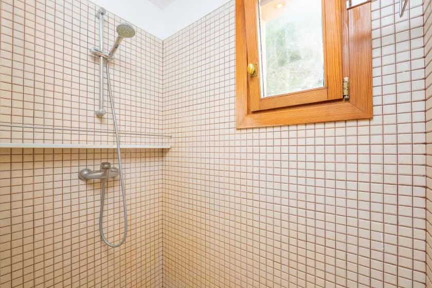 A tiled bathroom shower area with a wooden-framed window.