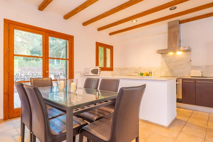A dining area with a glass table and an open kitchen behind it.