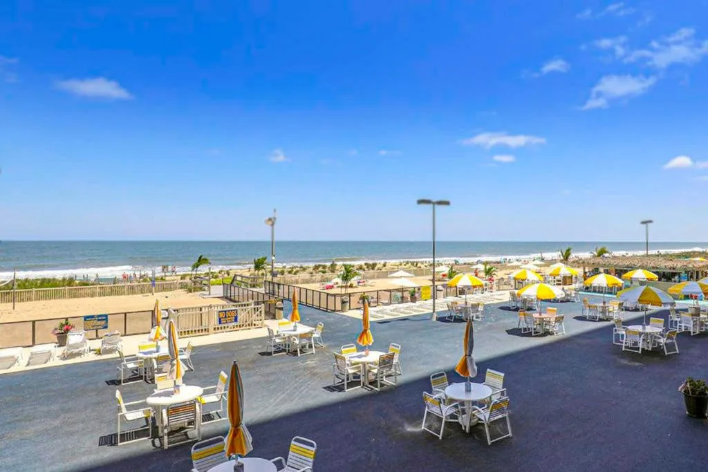 A seaside dining terrace has outdoor tables and seating overlooking the beach.