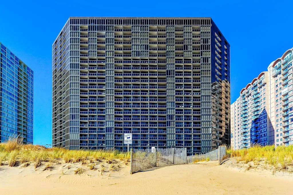Un alto edificio de apartamentos se alza detrás de una duna de arena.